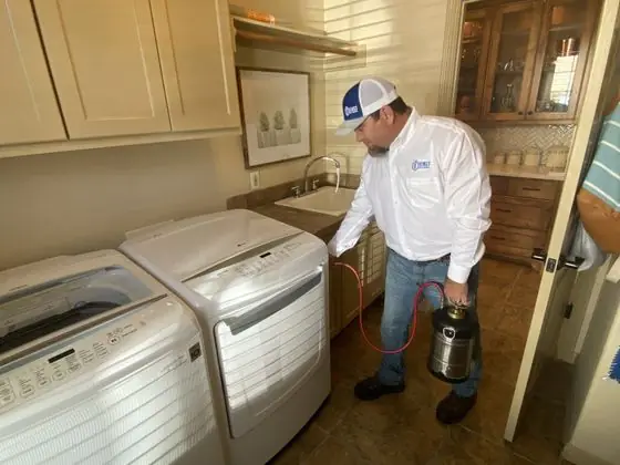 A King's Pest Control technician treating a home laundry room with a hand sprayer